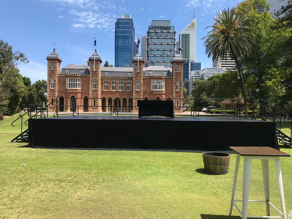 Black-skirted event stage on a city lawn in front of a heritage building