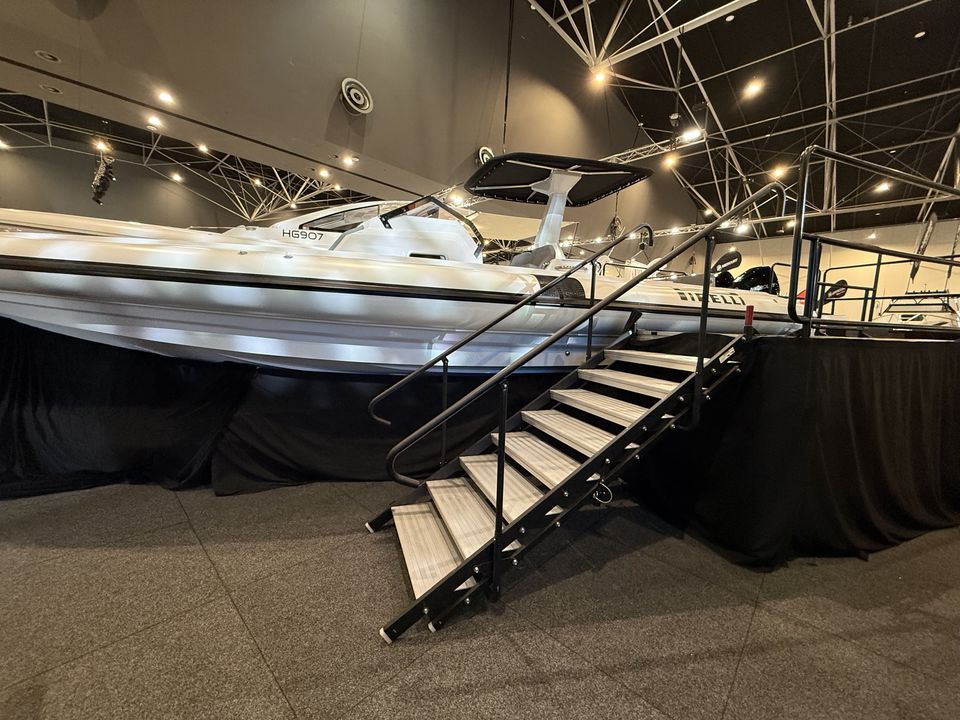 Boat on a raised display stage with stairs and handrails, with black skirting below