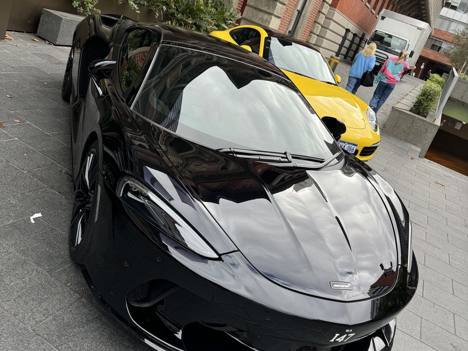 Black sports car on display on a paved street, with a yellow sports car behind