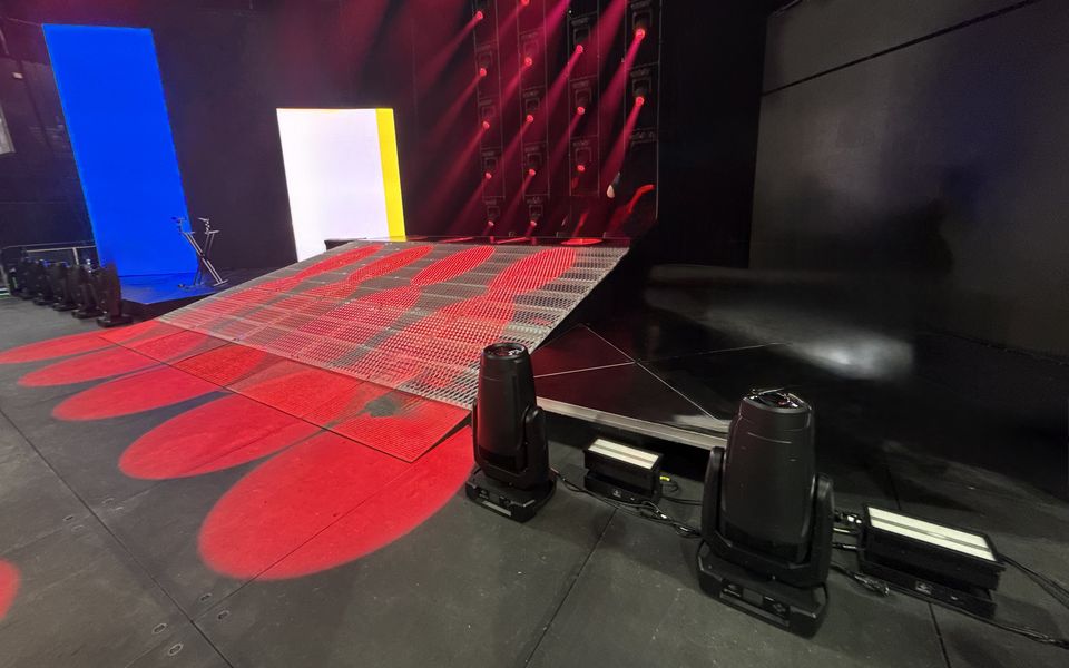 Silver mesh stage deck with angled edges under red concert lighting