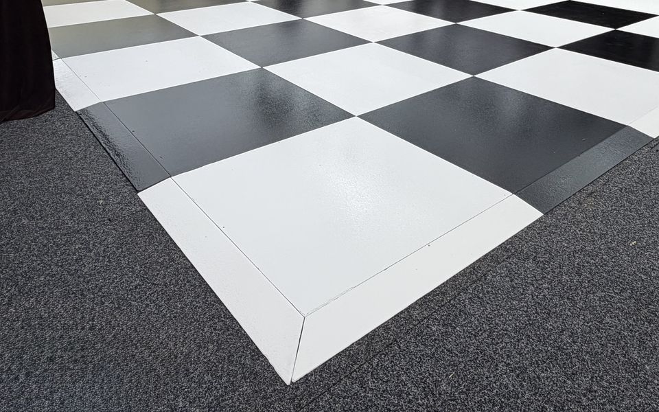 Black and white checkered dance floor with white edge trim, laid on carpet inside a marquee