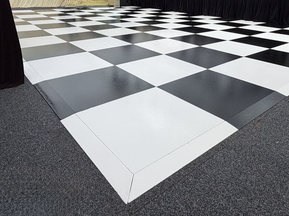 Black and white checkered dance floor with white edge trim, laid on carpet inside a marquee
