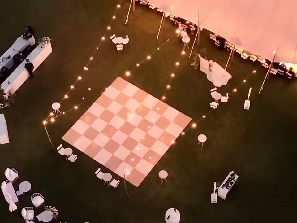 Aerial night view of a pink and white checkered dance floor beside sailcloth tents, ringed by festoon lights