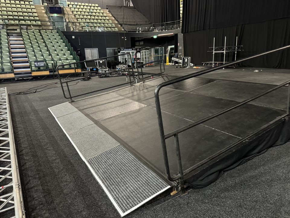 Access ramp with handrails leading onto a black stage in an indoor arena