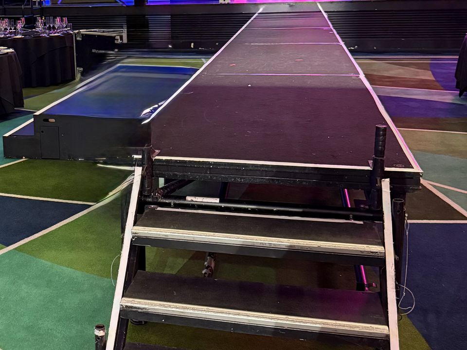 Aluminium step unit leading up onto a long black runway towards a lit stage at a gala dinner