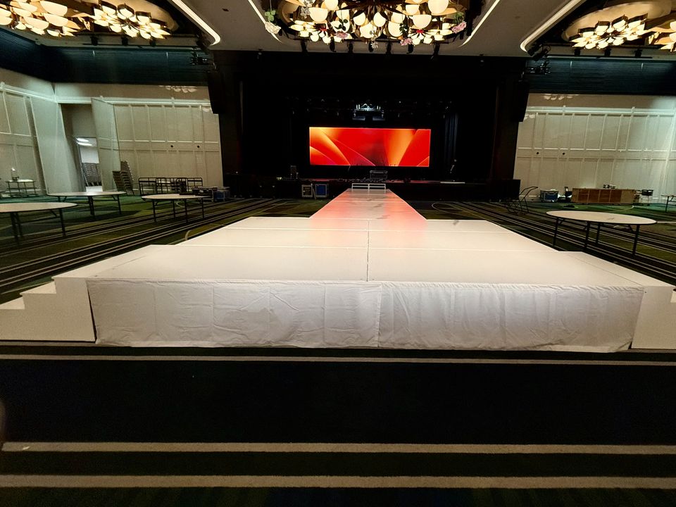 White stage with built-in white side steps and a runway leading to an LED screen in a ballroom