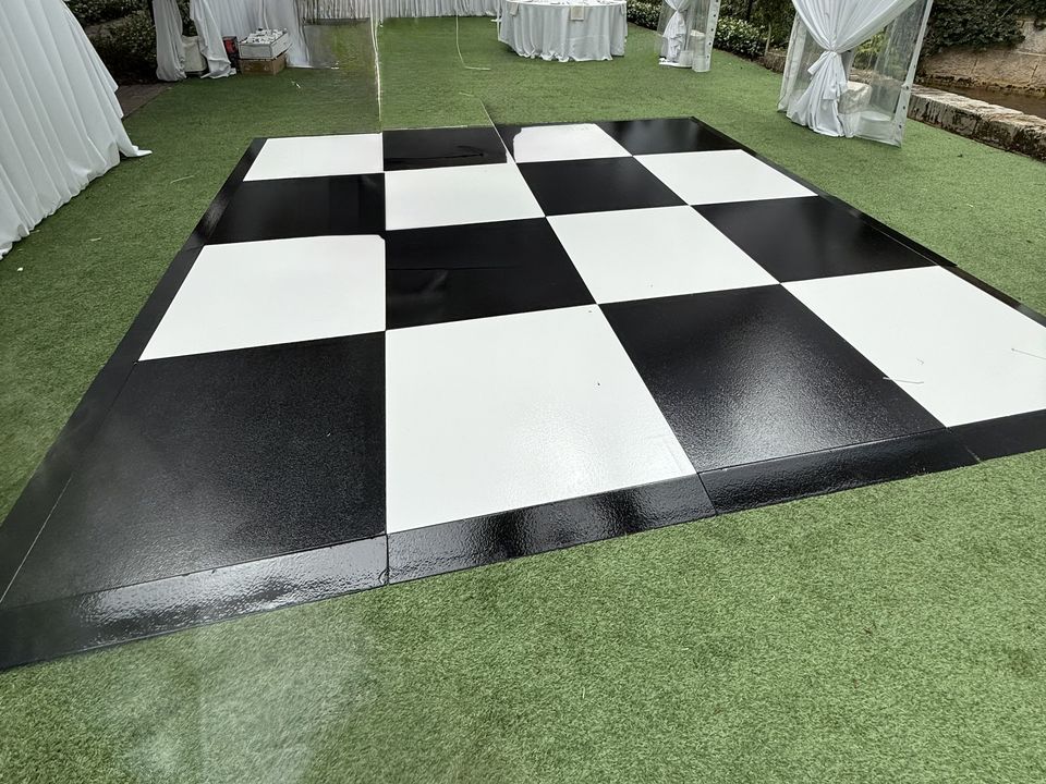Black and white checkered dance floor on turf inside a clear-roof marquee with white drapes