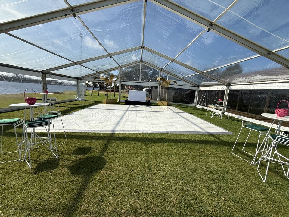 White dance floor on grass inside a clear-roof marquee beside the river