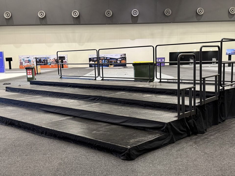 Wide black carpeted steps with handrails leading up to a platform in an exhibition hall