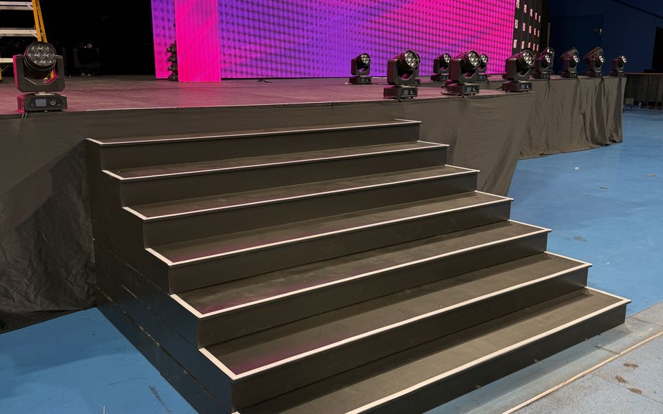 Wide black stage steps with LED edge lighting leading up to a stage with a pink LED wall